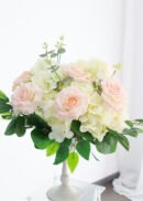 Eucalyptus Ficus Birch Faux Leaves with UV protection arranged in a white vase on a clear stand, displayed against a bright, white background.