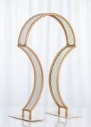 The 4 Pack Bridge Style Tabletop Centerpiece in matte gold features two symmetrical metal arches with a mesh pattern on rectangular bases, standing 31½" tall—ideal for tabletop display against any backdrop.