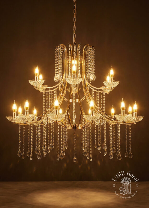 The 3ft Gold 18-Light Crystal Chandelier—2-Tier Curved-Arm Candelabra with crystal bowls, draped strands & teardrop pendants—shines against a dark brown background. The UBLZ floral logo is in the bottom right corner.