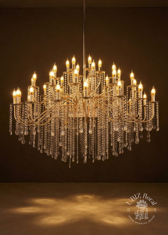 The 4.2ft Gold 44-Light Metal Crystal Chandelier—an extra-large multi-arm candelabra with cascading crystal strands and teardrop pendants—glows elegantly in a dark setting, with the UBIZ Floral logo in the lower right corner.