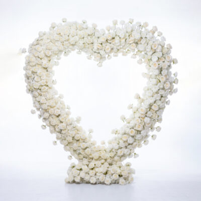 Large heart-shaped floral arrangement made entirely of white roses, standing on a white base against a bright, softly lit background.