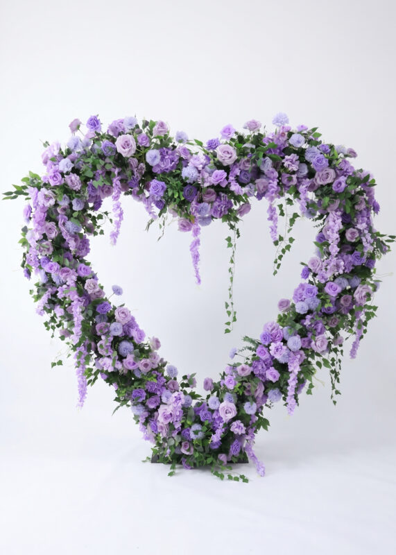 The Ombre Rose Heart Flower Backdrop is a luxury, 6.6ft freestanding floral arch in purple and lavender hues with green leaves, perfect for wedding proposals. It features a cloth backside and comes without a stand, shown against a white background.