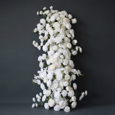 A vertical arrangement of numerous white roses and small white flowers is set against a dark gray background. The flowers cascade downward, creating a full and elegant floral display.