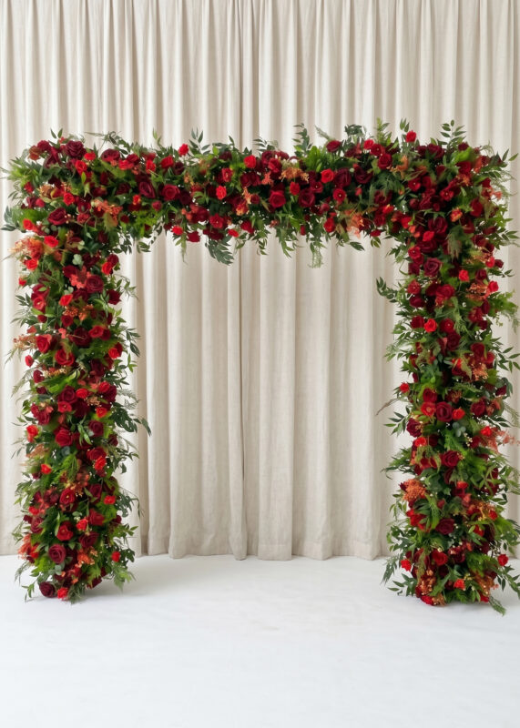 The Royal Blue Rose Flower Arch Backdrop, an elegant 8ft x 8ft roll-up floral cover, stands before floor-length cream curtains on a white floor, creating a dramatic setting for your wedding ceremony.