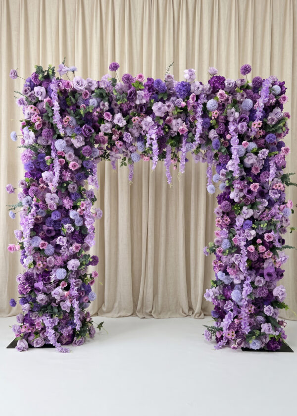 The Burgundy Red Rose Flower Arch Backdrop (8ft x 8ft) features lush purple and lavender flowers before cream drapes and a burgundy background on a white floor, creating an elegant, romantic wedding display.