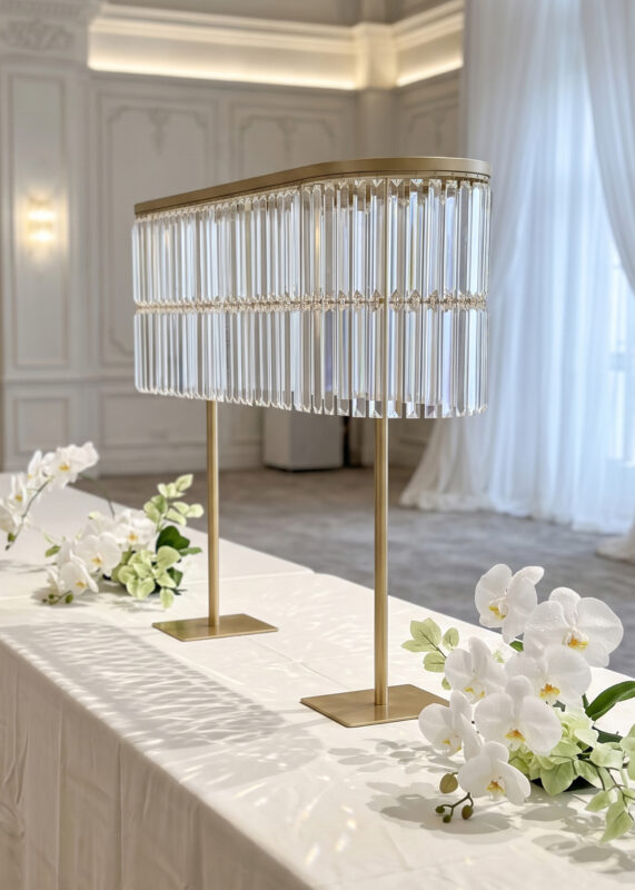 A 40in Gold Oval Crystal Fringe Centerpiece Stand, Dazzling & Elegant Double-Layer Wedding Table Decor with two tiers of dangling glass crystals, placed on a white tablecloth with orchid arrangements.