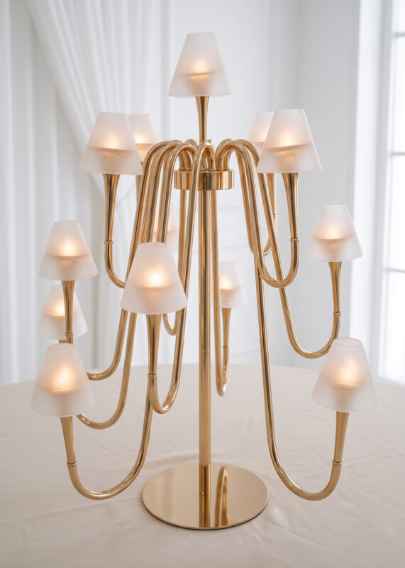 A gold multi-arm candelabra lamp with twelve glowing frosted glass shades sitting on a table.